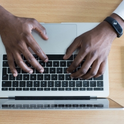 Black man typing on a laptop with a cell phone next to him.